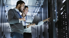 Two IT professionals review cloud servers in a dimly lit server room