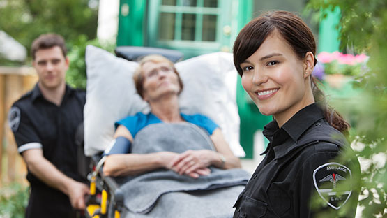 Female paramedic smiling with patient on a stretcher in the background